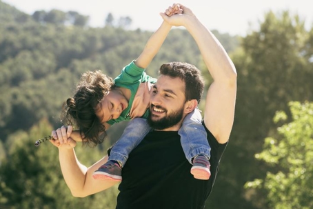 A father standing with his infant daughter sitting on his shoulders.