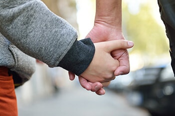 A parent with child custody holds their small child's hand